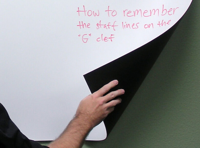 Memory aid for the G clef staff lines on a whiteboard Whiteboard with handwritten note about G clef staff lines and a person's hand lifting a black sheet.